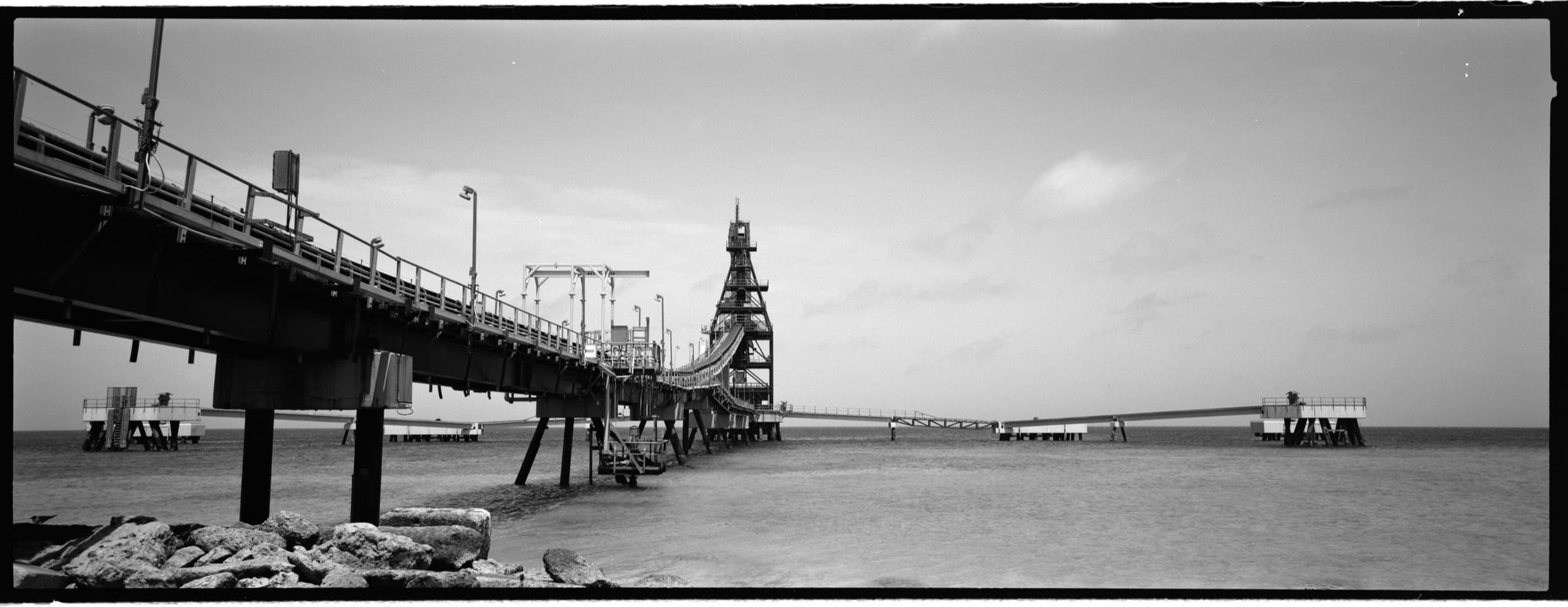 Black-and-white panoramic view of an industrial pier extending over water