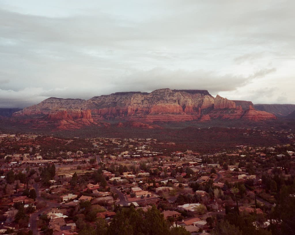 Town nestled in a valley beneath a red-rock mesa under overcast sky