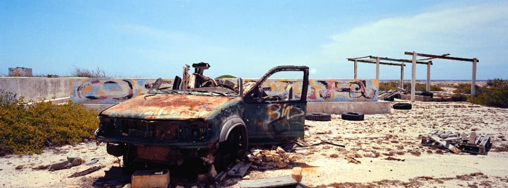 Burnt-out vehicle in front of a graffiti-covered wall in arid landscape