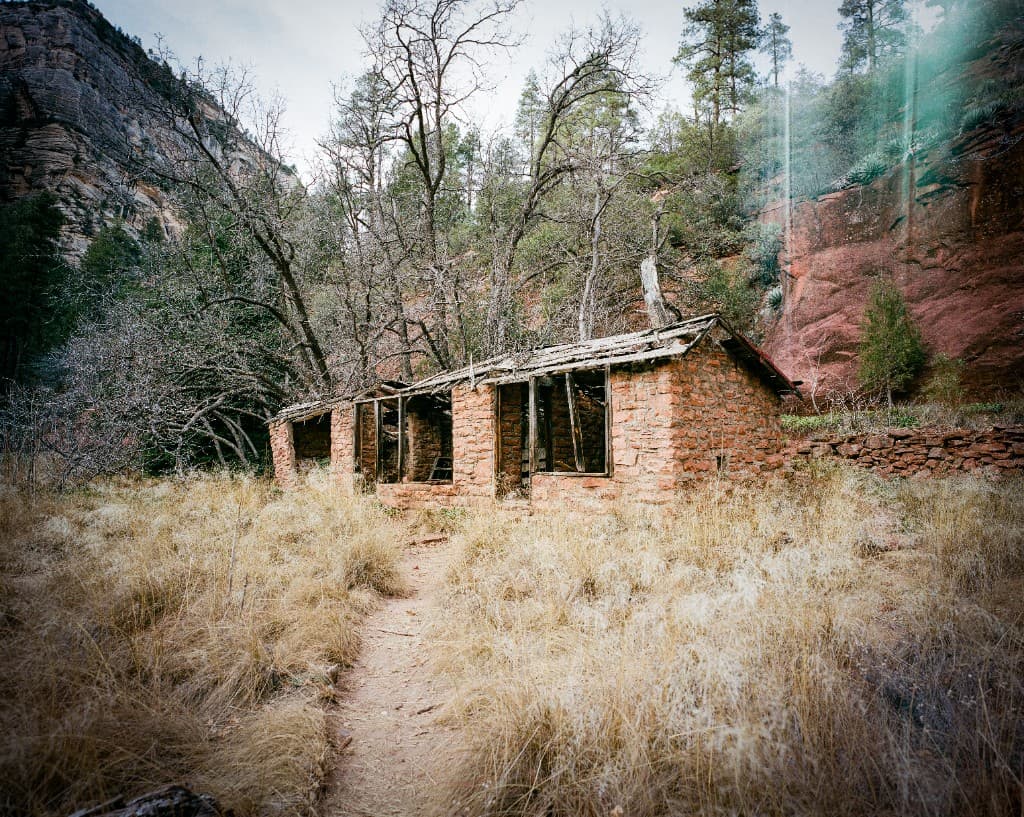 Abandoned stone cabin with collapsed roof against red canyon cliffs