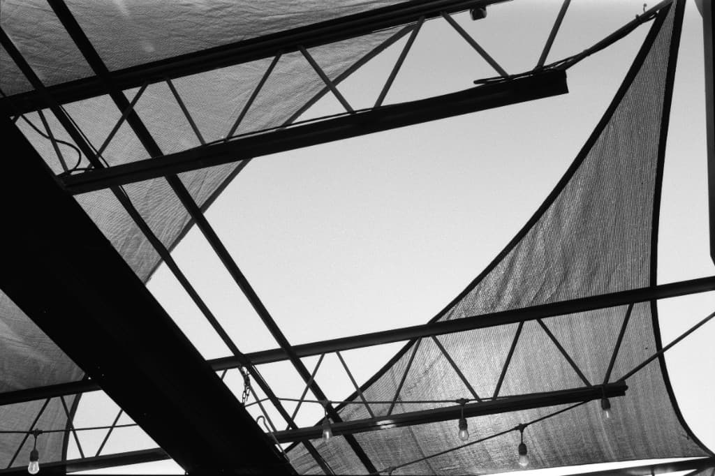 Looking up through geometric beams and fabric shade sails